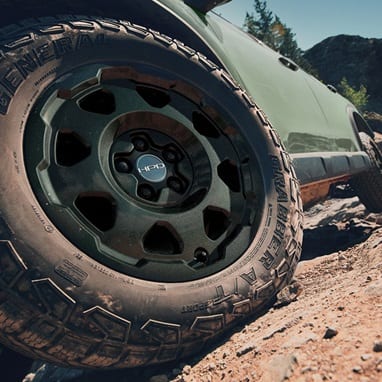 2027 Honda Passport TrailSport Elite in Ash Green Metallic profile on rocky terrain with black HPD wheels (Mid-Size SUV).
