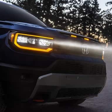 2027 Honda Passport TrailSport Elite in Smoke Blue Pearl front outdoors at dusk with glowing headlights (Mid-Size SUV).