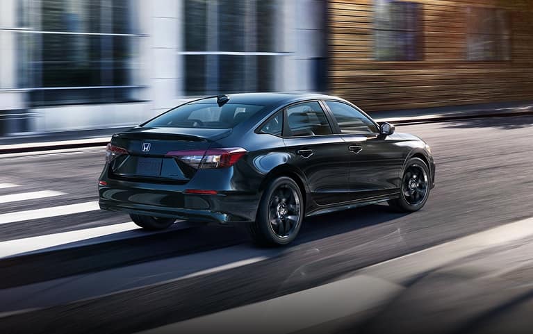 2027 Honda Civic Sedan Sport Hybrid in Crystal Black Pearl rear three-quarter view driving on a city street (Compact Sedan)